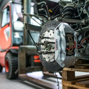 Detailed view of an automotive brake caliper and disc in an industrial workshop setting.